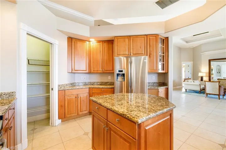 Kitchen with stainless steel fridge with ice dispenser, light tile patterned floors, light stone counters, glass insert cabinets, and brown cabinets