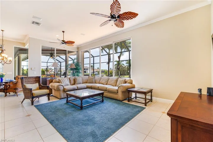 Living area featuring light tile patterned floors, crown molding, a ceiling fan, a chandelier, and baseboards