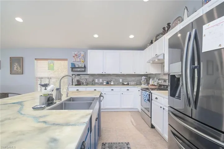 Kitchen with white cabinetry, light tile patterned flooring, decorative backsplash, sink, and appliances with stainless steel finishes