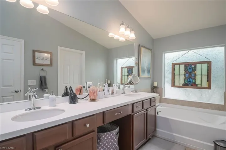 Bathroom with dual vanity, a bathing tub, and lofted ceiling