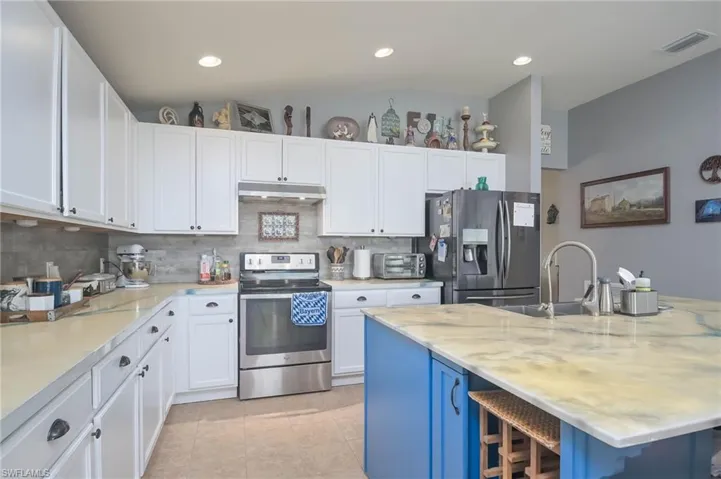 Kitchen with a breakfast bar area, tasteful backsplash, light tile patterned floors, an island with sink, and appliances with stainless steel finishes