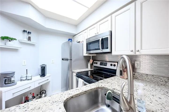 Kitchen featuring stainless steel appliances, tasteful backsplash, white cabinets, light stone counters, and open shelves