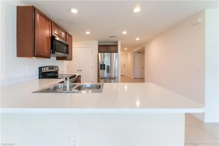 Kitchen with sink, light stone counters, stainless steel appliances, and light tile patterned floors