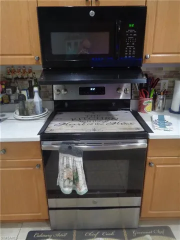 Kitchen featuring black microwave, backsplash, stainless steel electric range, and light tile patterned floors