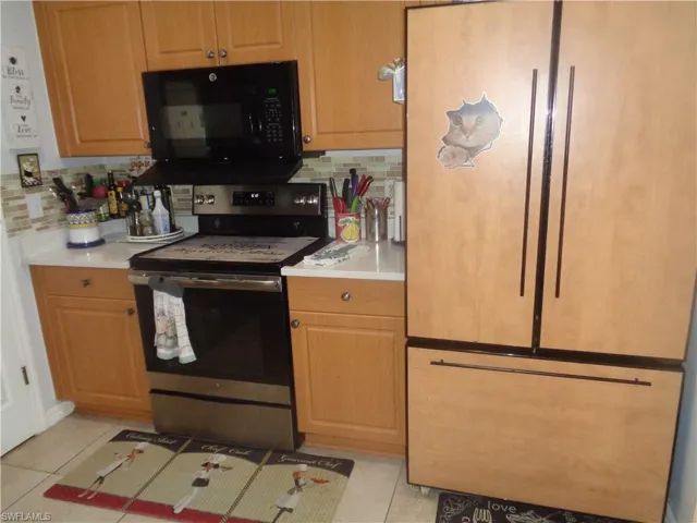 Kitchen featuring stainless steel electric range, black microwave, light countertops, and paneled refrigerator