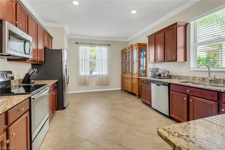 Kitchen with ornamental molding, a sink, light stone countertops, and appliances with stainless steel finishes