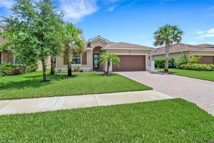 Ranch-style home featuring a tiled roof, decorative driveway, a garage, a front lawn, and stucco siding