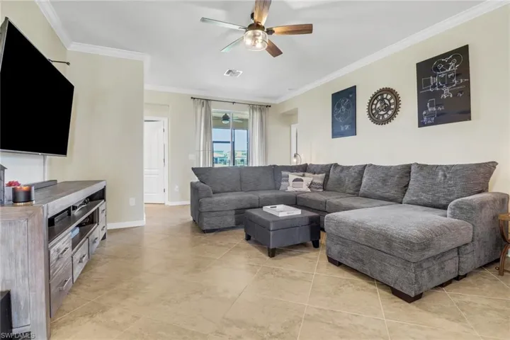 Living room featuring light tile patterned flooring, visible vents, baseboards, ornamental molding, and a ceiling fan