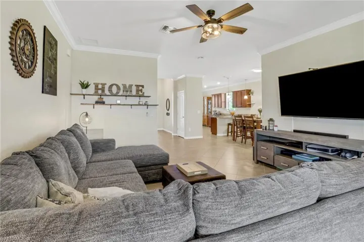 Living room featuring visible vents, crown molding, baseboards, ceiling fan, and light tile patterned floors
