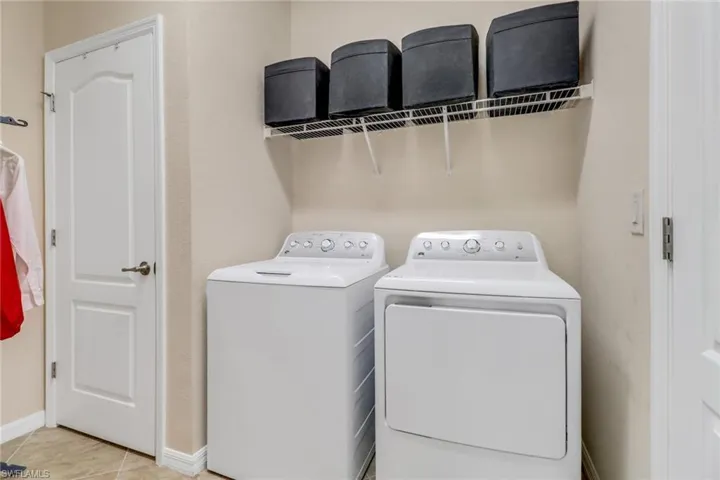 Clothes washing area with light tile patterned floors, washer and clothes dryer, baseboards, and laundry area
