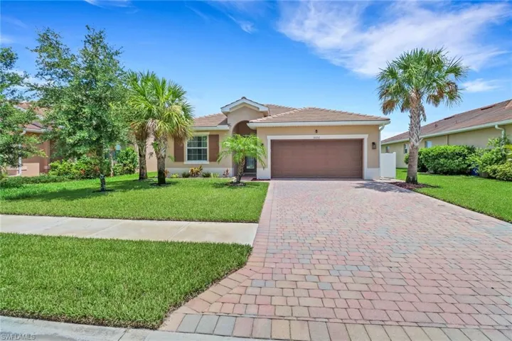 View of front of property featuring a tile roof, stucco siding, decorative driveway, a front lawn, and a garage