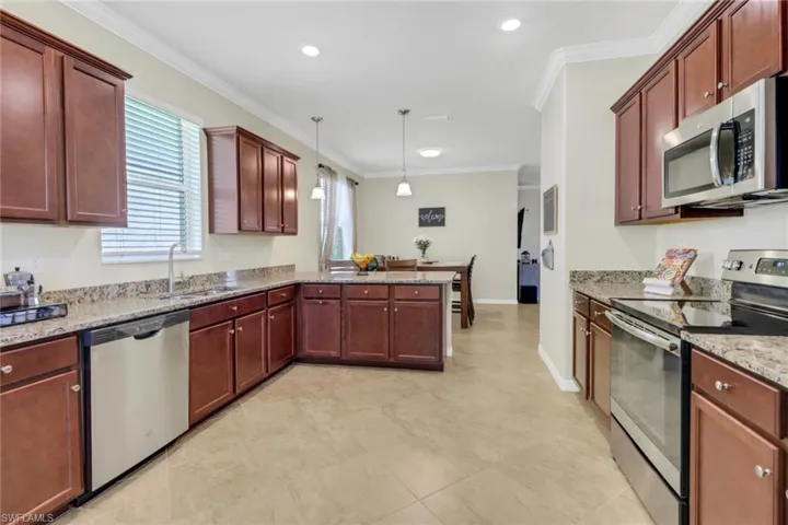 Kitchen featuring a sink, light stone countertops, a peninsula, stainless steel appliances, and ornamental molding