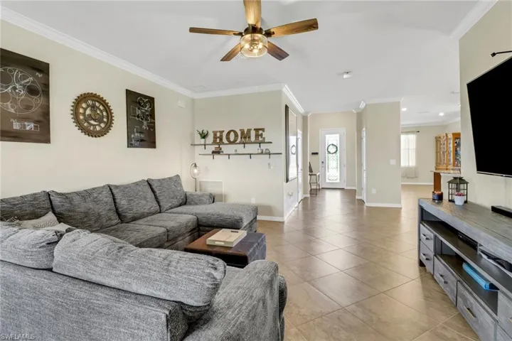 Living area featuring light tile patterned floors, a ceiling fan, and crown molding