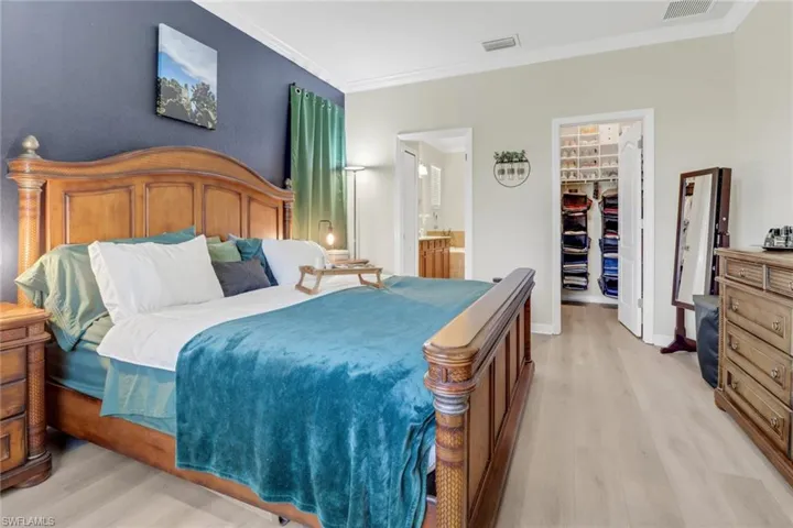 Bedroom with a spacious closet, ornamental molding, light wood-style floors, and visible vents