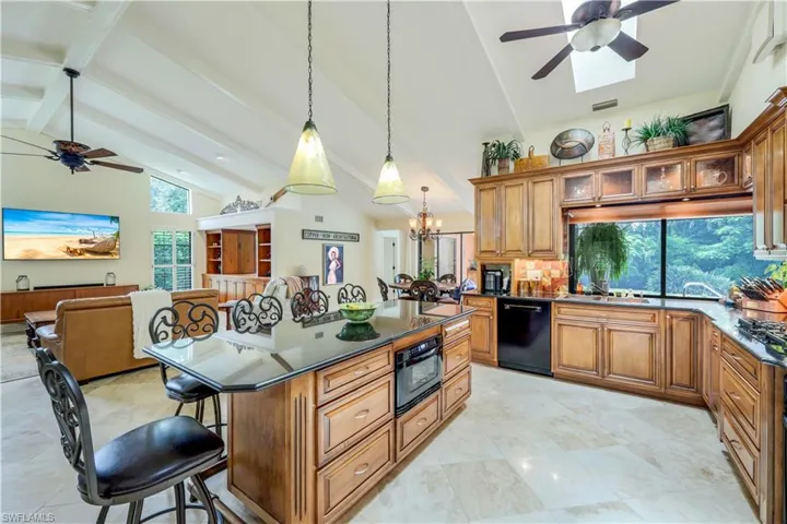Kitchen featuring light tile patterned flooring, black appliances, ceiling fan with notable chandelier, beam ceiling, and a breakfast bar area
