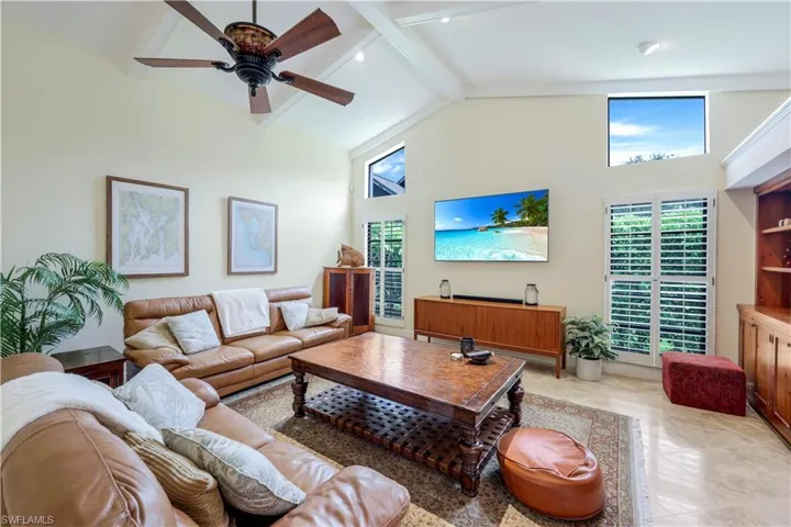 Tiled living room featuring ceiling fan, beam ceiling, and high vaulted ceiling