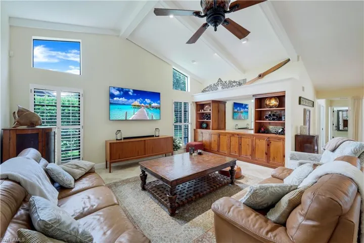 Living room featuring built in shelves, beam ceiling, ceiling fan, and high vaulted ceiling