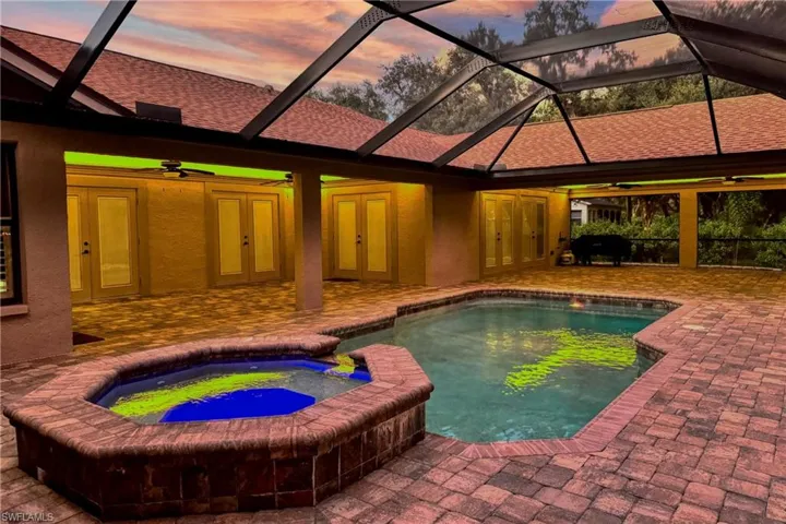 Pool at dusk featuring a lanai, ceiling fan, an in ground hot tub, french doors, and a patio area
