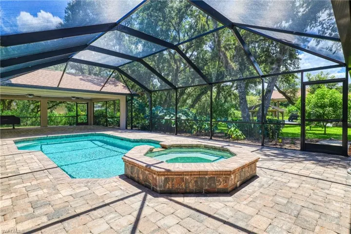 View of swimming pool featuring glass enclosure, a patio, and an in ground hot tub