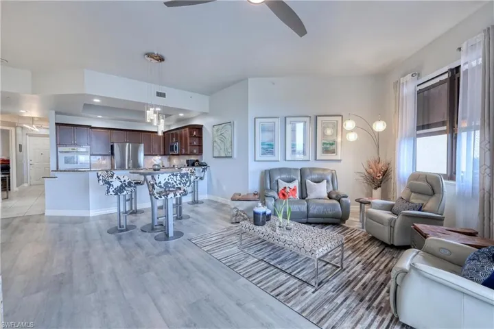 Living room with light hardwood / wood-style flooring, ceiling fan, and a raised ceiling