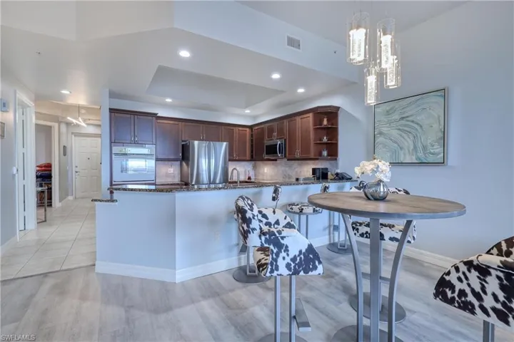 Kitchen with dark stone countertops, stainless steel appliances, hanging light fixtures, decorative backsplash, and a raised ceiling