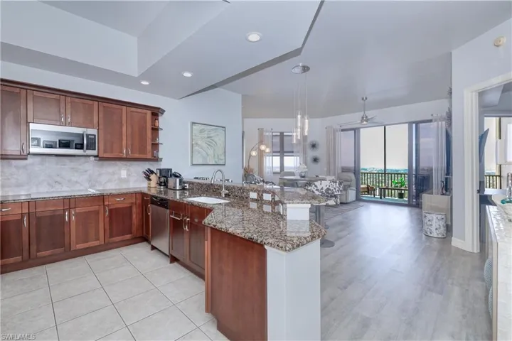 Kitchen with light hardwood / wood-style flooring, kitchen peninsula, stainless steel appliances, stone counters, and sink