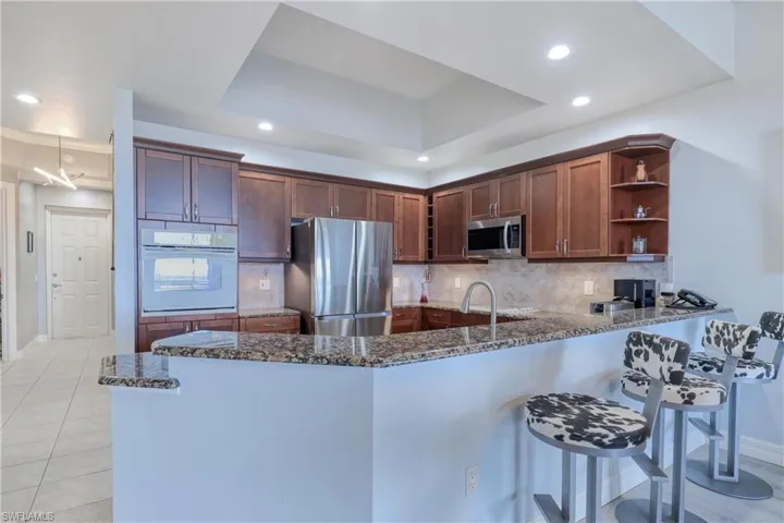 Kitchen featuring appliances with stainless steel finishes, dark stone countertops, kitchen peninsula, and a tray ceiling