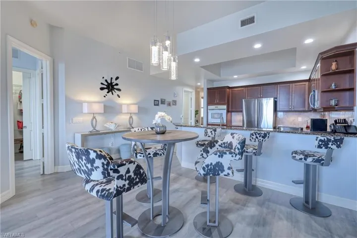 Kitchen featuring stainless steel appliances, pendant lighting, decorative backsplash, a raised ceiling, and light hardwood / wood-style flooring