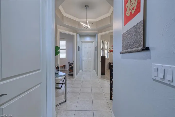 Hall with plenty of natural light, light tile patterned flooring, crown molding, and a tray ceiling