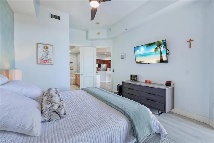 Bedroom with ensuite bath, light wood-type flooring, ceiling fan, and stainless steel refrigerator