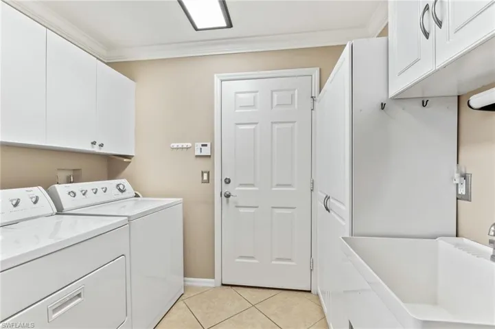 Laundry room featuring washing machine and dryer, light tile patterned flooring, crown molding, and cabinet space