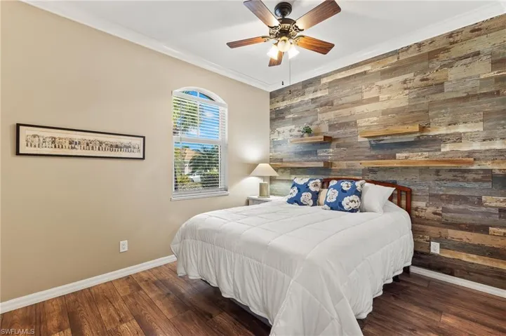 Bedroom with wood walls, ornamental molding, wood finished floors, an accent wall, and a ceiling fan