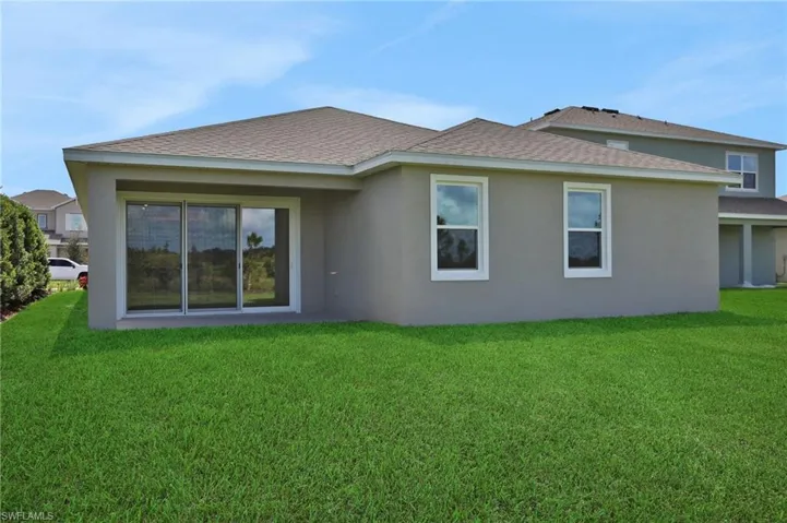 Rear view of house featuring roof with shingles, stucco siding, and a yard