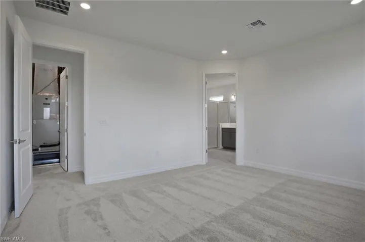 Unfurnished bedroom with light colored carpet, recessed lighting, connected bathroom, and heating unit
