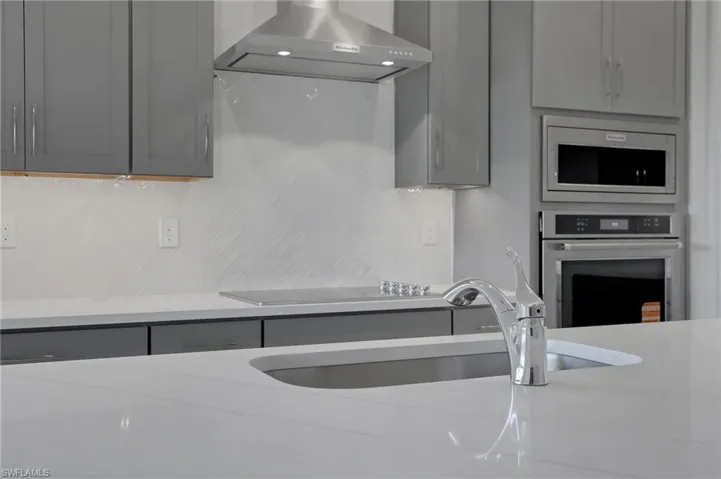 Kitchen with gray cabinets, light stone counters, stainless steel appliances, and backsplash