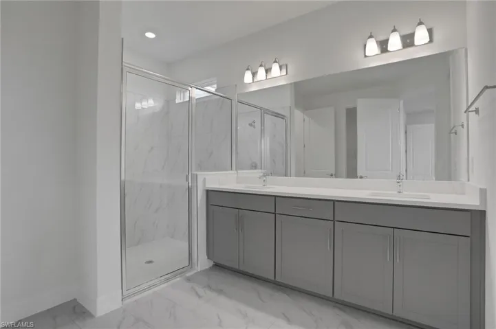 Full bathroom featuring double vanity, light marble finish floors, a marble finish shower, and recessed lighting