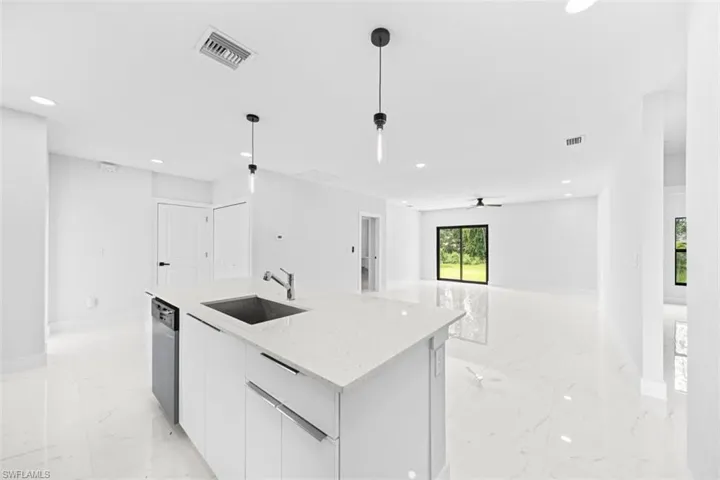 Open-concept living area featuring a kitchen island with sink, white shaker cabinetry, stainless steel appliances, and large format tile flooring