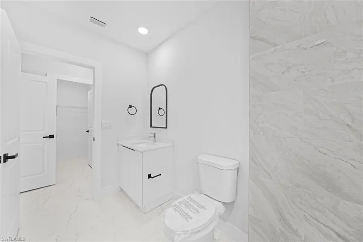 White vanity with a single basin sink, wall-mounted mirror, and contemporary black fixtures