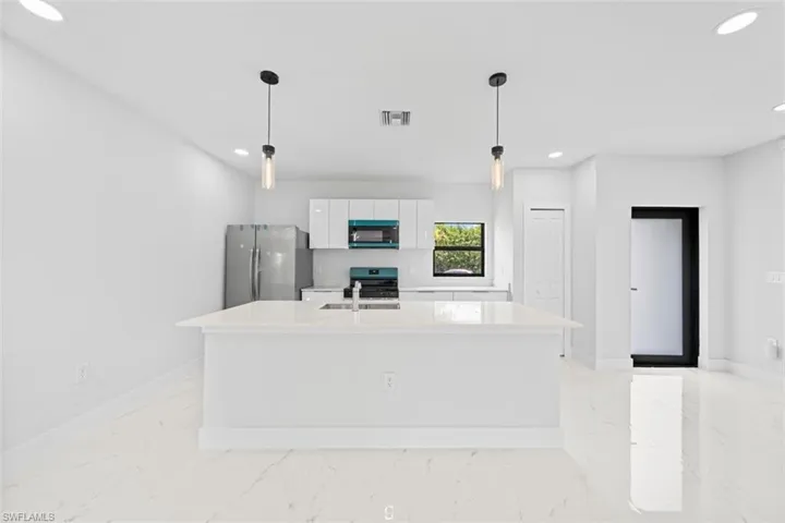 Open-concept kitchen with a central island, recessed lighting, stainless steel appliances, and a window providing natural light
