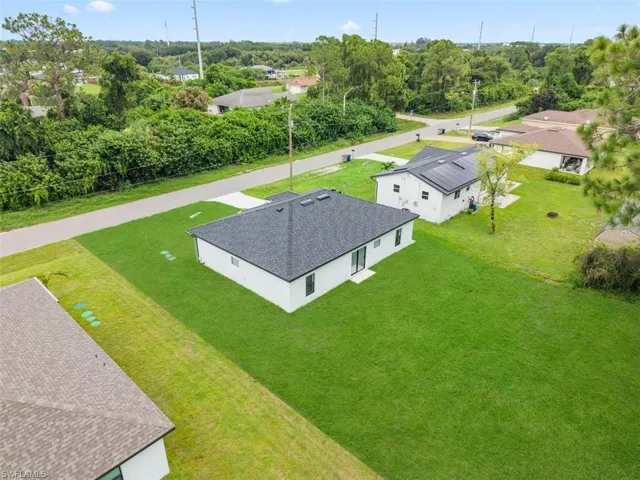 White exterior with dark roof, expansive green lawn, and paved driveway