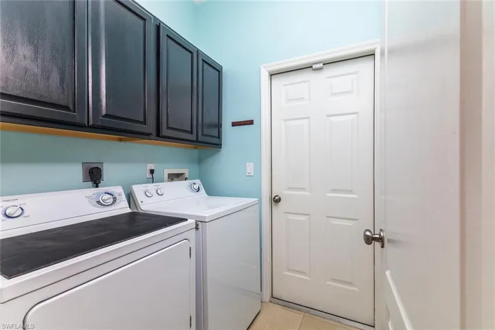 Laundry room with cabinets, electric dryer, and washer machine, and light tile floors