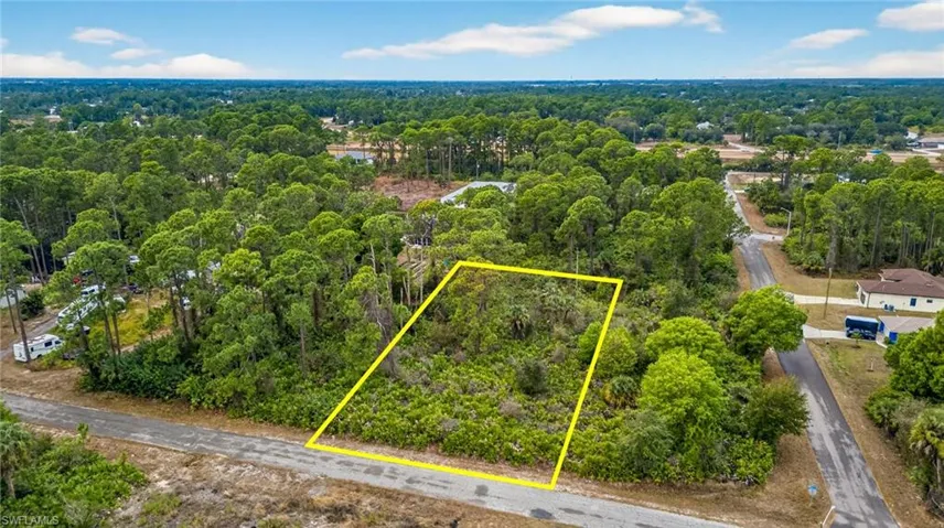 Aerial view of property and surrounding area featuring property parcel outlined and a heavily wooded area
