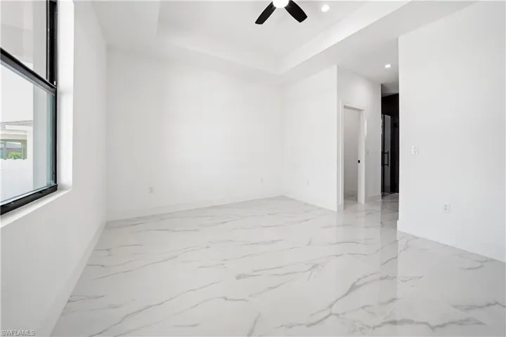 Spacious room featuring large format tile flooring, a tray ceiling, recessed lighting, and a ceiling fan