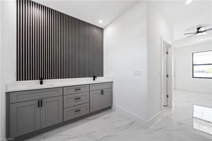 Dual basin vanity with a decorative slatted accent wall, quartz countertop, and matte black fixtures