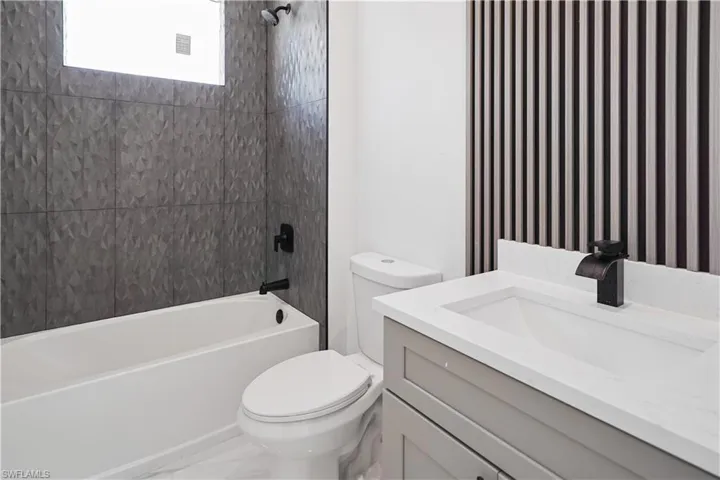 Bathroom featuring a textured gray tile shower surround, a white bathtub, and a modern vanity with an integrated sink and dark bronze faucet