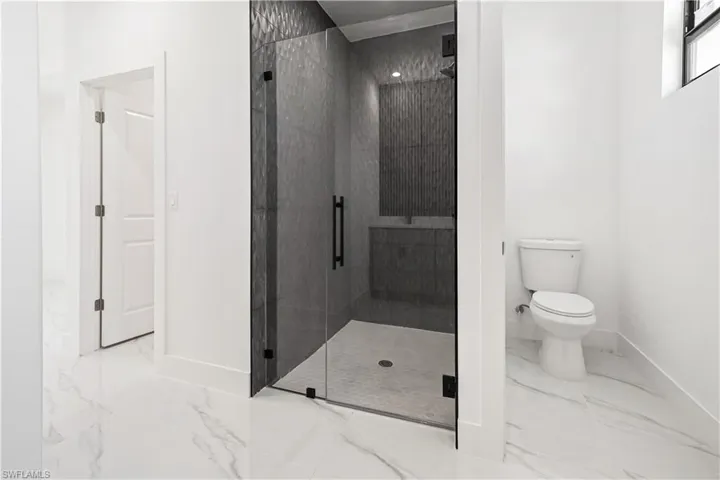 Walk-in shower with dark textured wall tile and a glass enclosure with matte black hardware