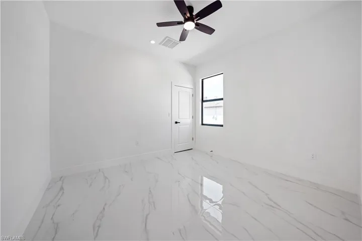 Spacious room featuring white walls, high ceilings, a contemporary ceiling fan, and large format marble-look flooring