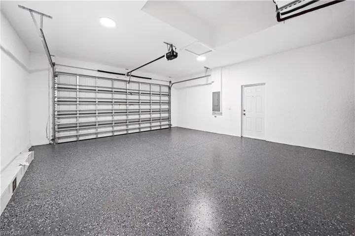 Spacious garage featuring a durable speckled epoxy floor, overhead lighting, an automatic garage door opener, and a side entry door