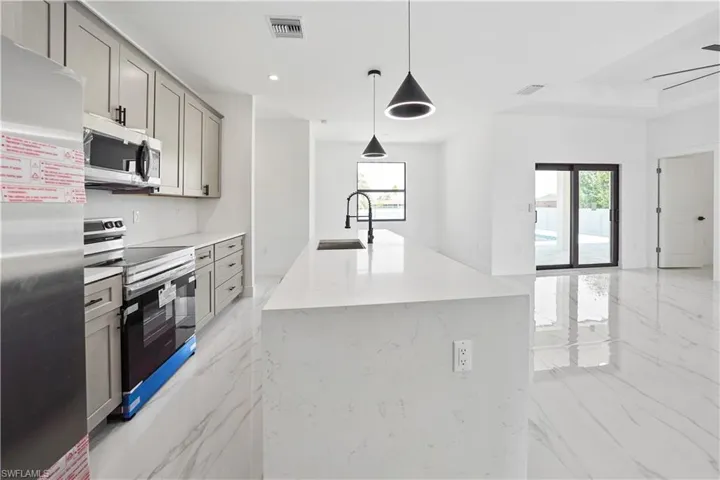 Kitchen featuring light gray cabinetry, stainless steel appliances, and a white countertop with an integrated sink and matte black faucet