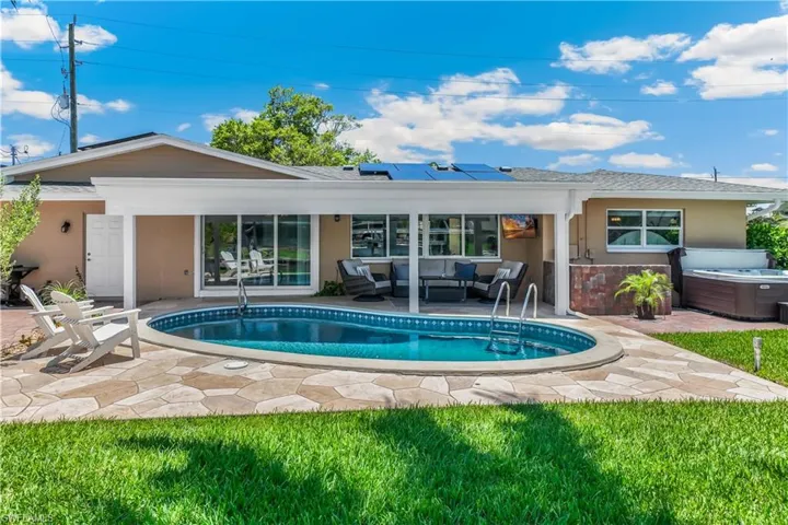 Rear view of property featuring a patio area, a hot tub, an outdoor hangout area, and solar panels